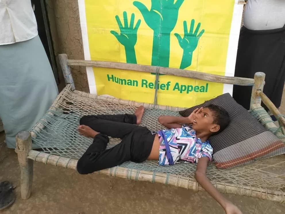 Child resting on a bed in front of a Human Relief Appeal banner